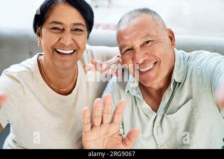 Mature couple, waving and selfie on home sofa for video call, streaming and internet. A happy man and woman together on a couch for social media Stock Photo
