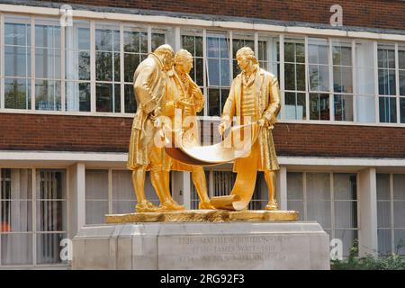 The newly gilded statue of Matthew Boulton, James Watt and William Murdoch, outside the House of Sport on Broad Street, Birmingham.  The statue is in bronze with a gold finish, and is by William Bloye.  It was unveiled in 1956.  The three men depicted were pioneers of the industrial revolution in the late 18th century, and they are shown discussing engine plans.  The statue has two local nicknames: The Golden Boys, and The Carpet Salesmen. Stock Photo