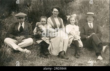 British Family Group pose for a photo - the two young daughters are proudly holding their favourite dolls. Stock Photo