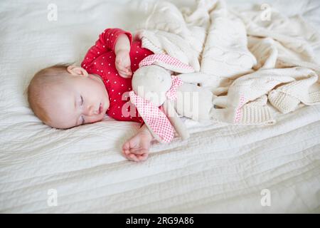 Baby girl sleeping under knitted blanket with her favorite toy. Little child in pink clothes having a day nap. Infant kid in nursery Stock Photo