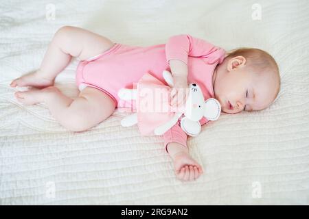 Baby girl having a nap with her favorite mouse toy. Little child sleeping on bed with comforter. Sleep training concept. Infant kid in sunny nursery Stock Photo