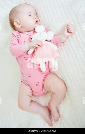 Baby girl having a nap with her favorite mouse toy. Little child sleeping on bed with comforter. Sleep training concept. Infant kid in sunny nursery Stock Photo