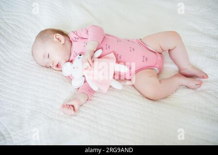 Baby girl having a nap with her favorite mouse toy. Little child sleeping on bed with comforter. Infant kid in sunny nursery Stock Photo