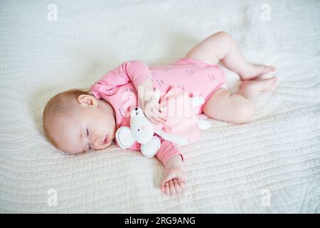 Baby girl having a nap with her favorite mouse toy. Little child sleeping on bed with comforter. Sleep training concept. Infant kid in sunny nursery Stock Photo