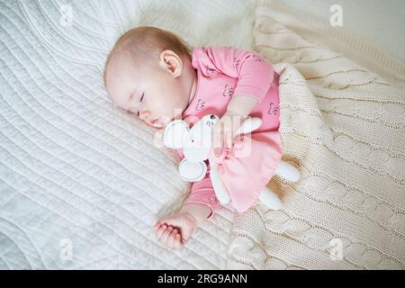 Baby girl having a nap with her favorite mouse toy. Little child sleeping on bed with comforter. Infant kid in sunny nursery Stock Photo