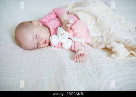 Baby girl having a nap with her favorite mouse toy. Little child sleeping on bed with comforter. Infant kid in sunny nursery Stock Photo