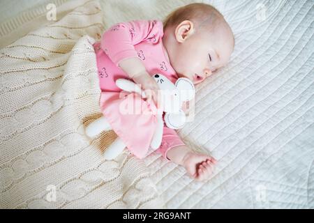 Baby girl having a nap with her favorite mouse toy. Little child sleeping on bed with comforter. Infant kid in sunny nursery Stock Photo