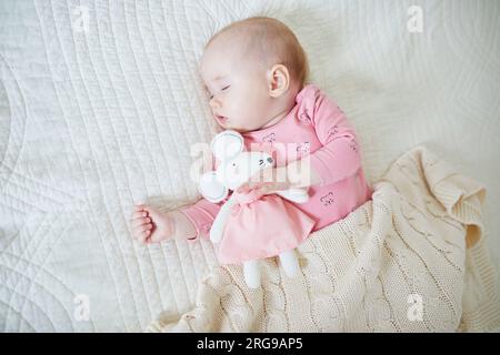 Baby girl having a nap with her favorite mouse toy. Little child sleeping on bed with comforter. Infant kid in sunny nursery Stock Photo