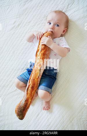 Six months old baby girl eating traditional French bread (baguette). Introducing solids to infant kids. Baby-led weaning concept Stock Photo