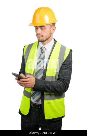 Portrait of a business man in a suit, with a hi-vis vest & hardhat reading a message on a mobile phone Stock Photo