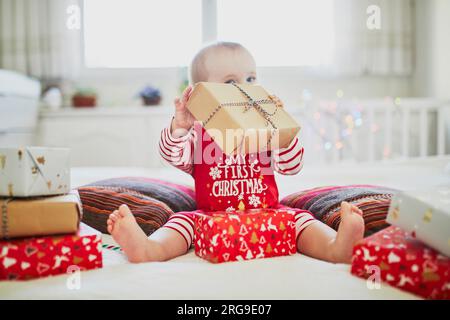 Happy little baby girl wearing pyjamas opening Christmas presents on her very first Christmas. Celebrating Xmas with kids at home Stock Photo