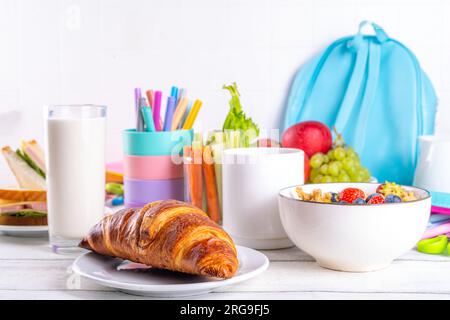 Healthy nutritious  morning breakfast for school kids, with fresh fruits, vegetables, croissant, muesli, milk and sandwich. Having breakfast before sc Stock Photo