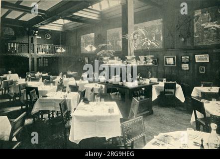 Photograph of what is described as a 'high-class' restaurant in Britain during the Edwardian era. The room is slightly baronial in style with wood panelling and studded dining chairs. Note the pristine white tablecloths and murals on the wall. Stock Photo