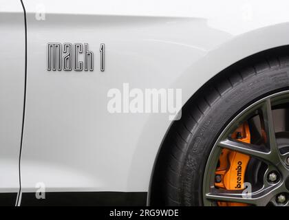 A close-up of the front right wing of a white Ford Mustang Mach 1 American muscle car showing the Mach 1 lettering, tyre, alloy and Brembo brake pads Stock Photo