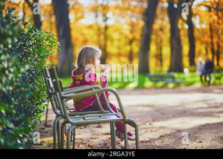 Adorable little girl in pink knitted poncho walking in Luxembourg garden on a sunny fall day. Happy child having fun outdoors on a street of Paris, Fr Stock Photo