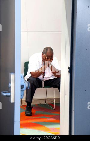 african american security guard in uniform holding head in hands, through doorway concept for boredom depression contemplation Stock Photo