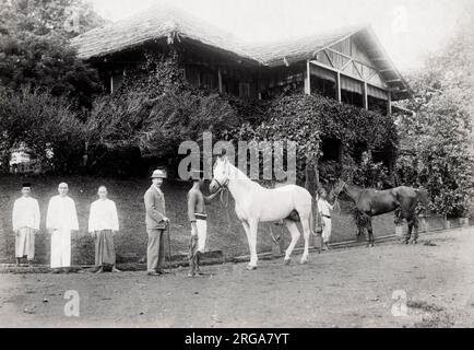 British man with his servants and horses outside his bungalow, late 19th century SE Asia, possibly Singapore Stock Photo