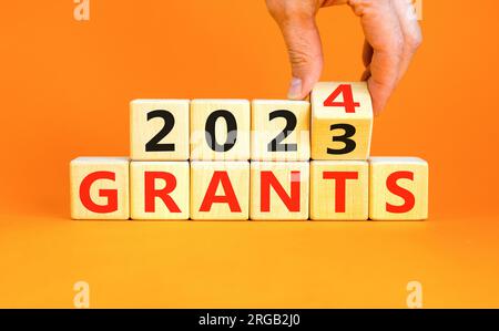 Planning 2024 grants new year symbol. Businessman turns a wooden cube and changes words Grants 2023 to Grants 2024. Beautiful orange background, copy Stock Photo