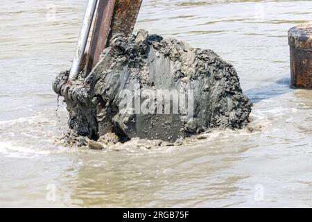 Dredging the bottom of water area, view of the bucket of the floating excavator full of mud Stock Photo