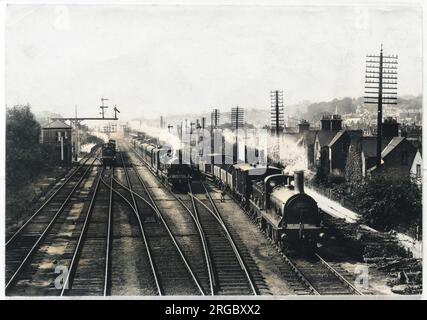 A goods train waits on one track to let the passenger train go through, while a third train approaches through the station at Redhill, Surrey. Stock Photo