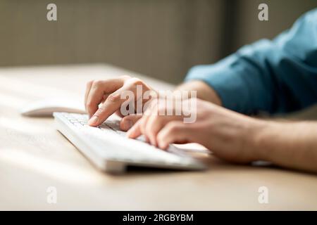 Unrecognizable man typing on computer keyboard while sitting at desk Stock Photo