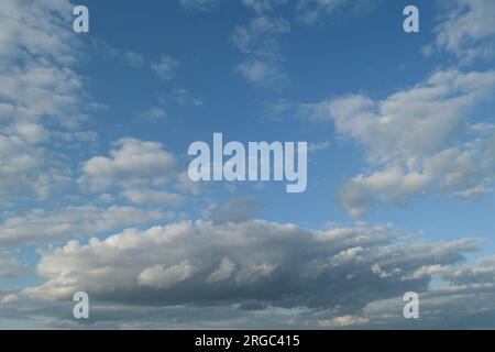 Dark grey and white clouds seen against a blue sky during the day in summer. Stock Photo