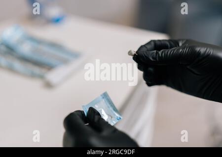 Detail cropped shot of unrecognizable female dentist in rubber gloves opening package with new nozzle for polishing and grinding teeth of patient. Stock Photo