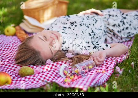 Beautiful young woman having picnic in parc, lying on her back with fruits around her Stock Photo