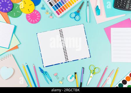 Back to school background. Colored pencils, books, notebooks, pens, watercolor paint, scissors, math fractions, calculator on pastel green background Stock Photo