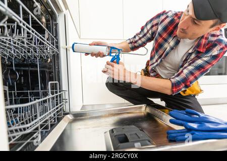 Worker using screwdriver to repair dishwasher at home stock photo Stock Photo