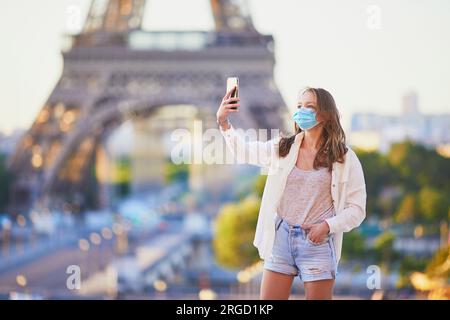 Girl standing near the Eiffel tower in Paris and wearing protective face mask. Tourist spending vacation in France during pandemic Stock Photo