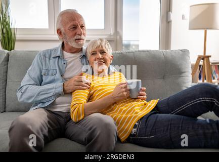 Cheerful senior couple sitting on sofa at home, relaxing together and smiling Stock Photo