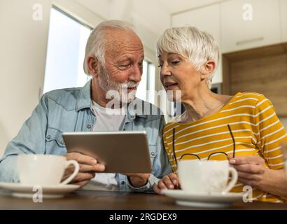 Senior couple sitting at dining table and looking at tablet, surfing internet Stock Photo