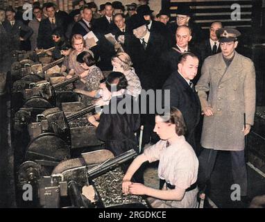 King George VI being given a tour of inspection of a Royal Ordnance factory and seeing at first-hand the immense effort being put in to produce arms, in this case anti-aircraft and anti-tank guns.  Picture shows the King watching some of the women workers in the factory sorting ammunition. Stock Photo