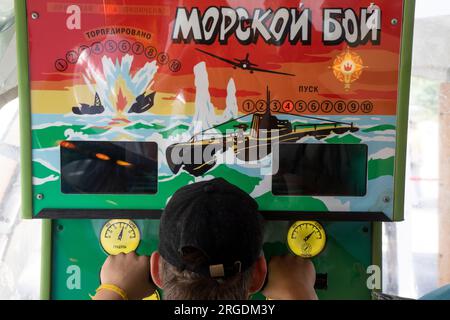 Moscow, Russia. 5th of August, 2023. A young man plays on a popular Soviet slot machine 'Sea Battle' in the pavilion of VDNKh exhibition centre in Moscow, Russia. The Russian words read 'Sea Battle' Stock Photo