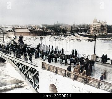 View of a bridge over which a locomotive is being pulled by fourteen horses to be delivered to the Orlovsko-Kitebskaya line. Crowds of people have gathered in the snow to watch it go by. Stock Photo