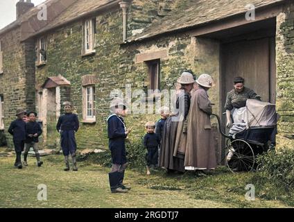 Scene in a village street, with women gathered round a pram, and boys playing. Stock Photo