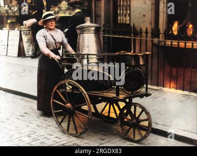 WW1 - Brighton, Sussex - A Milkmaid from Cowley's Dairy sells milk from a churn on a hand cart. The newspaper billboards in the background announce the exacuation of Warsaw, Poland - detailing that its bridges have been destroyed. Stock Photo