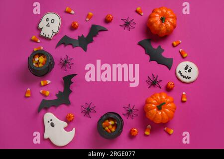 Frame made of tasty candy corns, cookies and Halloween decor on pink background Stock Photo