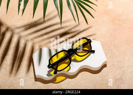 Decorative podium with stylish sunglasses and palm leaf on orange background Stock Photo