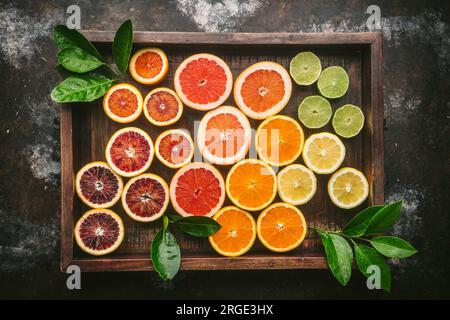 Citrus fruits (orange, blood orange, grapefruit, lemon, lime) cut in half and arranged by color in rustic wood box with fresh citrues leaves Stock Photo