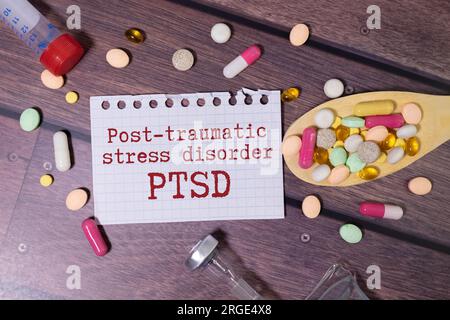 A wooden block with the word PTSD stands on a blue background among multi-colored pills. Medical concept Stock Photo