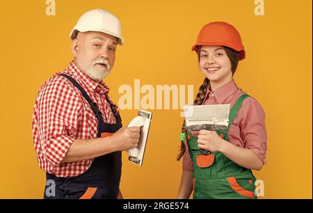 happy child and grandfather plasterer in hard hat on yellow background. Stock Photo