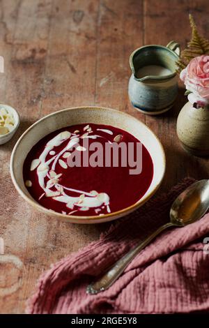 A bowl of beetroot soup with cream and almond flakes on a wooden table Stock Photo