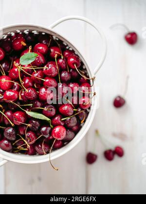 Fresh ripe cherries in white stainless steel colander. Top view of wet red cherry over white woden background. Shallow DOF. Cherries aestetic. Copy sp Stock Photo