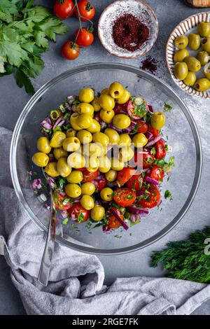 Chopped onions, green onions, parsley, dill, halved cherry tomatoes and pitted green olives in a glass bowl. Stock Photo
