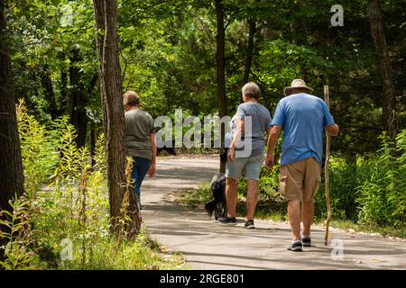 Two Caucasian women & a man walking with dog on a nature & exercise trail in Sedgwick County Park, Wichita, Kansas, USA. Stock Photo