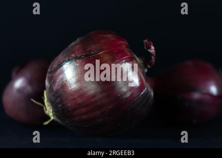 Picture of three red onions isolated on a black background. Red onions (also known as purple or blue onions in some mainland European countries) are c Stock Photo