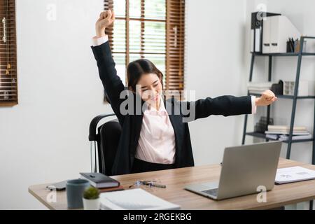Businesswoman raise arms to stretching for relaxation after exhausted from overworked in workplace. Stock Photo