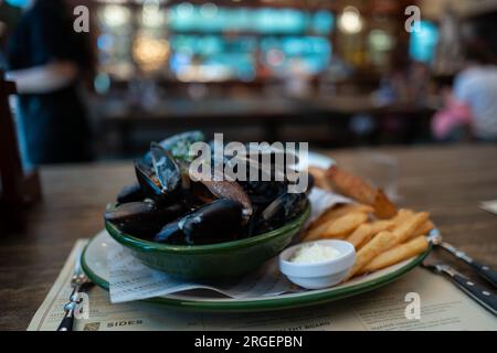 Mussels with herbs in a bowl with lemon and French fries on plate. Seafood along with sour cream. Stock Photo